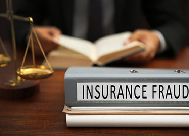 Binder labeled 'INSURANCE FRAUD' on desk with scales of justice and lawyer, symbolizing legal action.