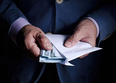 A person in a suit is holding an open envelope with US dollar bills inside, symbolizing financial transactions.