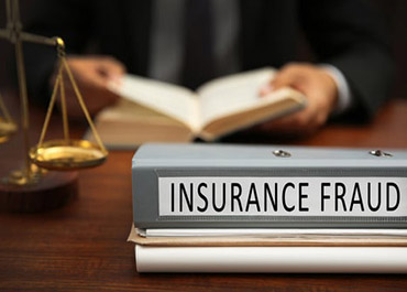 Binder labeled 'INSURANCE FRAUD' on desk with scales of justice and lawyer, symbolizing legal action.