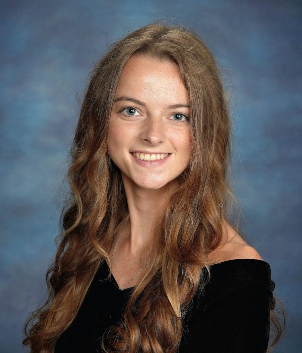 Young women with long, wavy brown hair smiling against a blue background represent the Community Leaders Scholarship