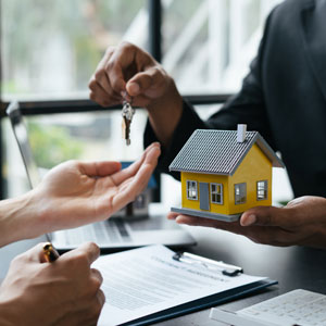 A real estate agent hands keys and a model house to a client, symbolizing a property transaction.