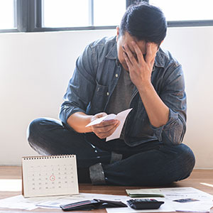 Distressed person sits on floor, surrounded by bills, with a calendar, symbolizing financial hardship.