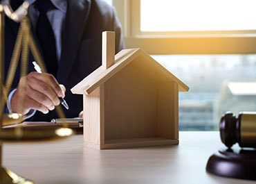 Lawyer with house model, scales, gavel. Expert in Dallas mortgage fraud and related wire fraud cases.