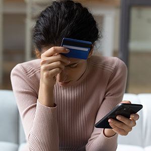 Person stressed, holding credit card and phone, symbolizing financial fraud.