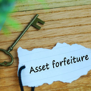 Key and 'Asset Forfeiture' paper on wood, symbolizing legal solutions for forfeiture.