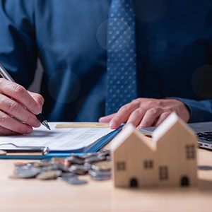 Person signing documents, coins, and model houses, symbolizing Dallas mortgage fraud legal aid.