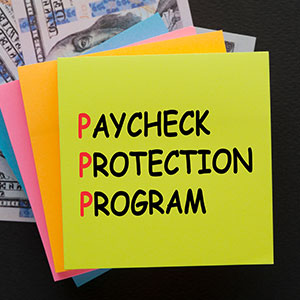 Green sticky note 'PAYCHECK PROTECTION PROGRAM' on dollar bills, symbolizing PPP loan fraud.