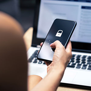 Person's hand on phone with lock icon, laptop in background, for online security.