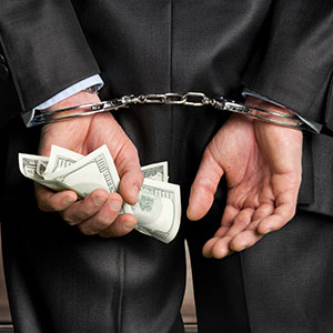 Man in suit, hands cuffed behind back, holding money, symbolizing white-collar crime defense.