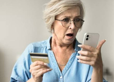 Shocked senior woman holding credit card and phone, illustrating unauthorized use and fraud.
