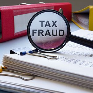Magnifying glass over 'TAX FRAUD' on documents, with binders, symbolizing a tax investigation.