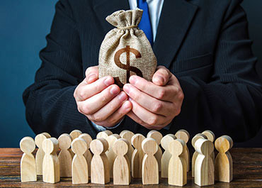 Businessman holds money bag above wooden figures, symbolizing financial power, distribution, or fraud.