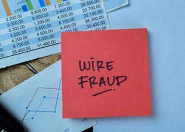 Red sticky note 'WIRE FRAUD' on financial documents, symbolizing fraudulent activity.