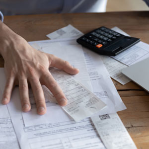 A hand sorts through receipts and papers on a desk with a calculator.